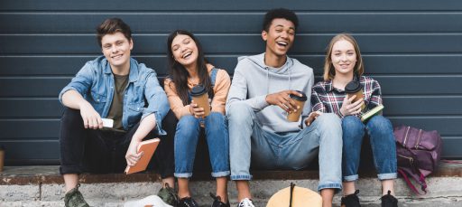 happy teenagers sitting, smiling, holding paper cups and looking at camera